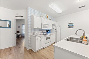 Una cocina moderna con armarios blancos, horno empotrado, microondas y pileta de acero inoxidable.