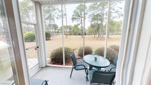 A covered patio with a table and chairs, a view of a grassy area with trees, and a door leading outside. - CH3702, Tee Off in Comfort, Perfect Golf Retreat (Sunset Beach)