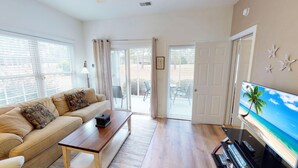 A living room with a sofa, coffee table, and a television displaying a beach scene. - CH3702, Tee Off in Comfort, Perfect Golf Retreat (Sunset Beach)