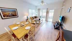 A dining area with a wooden table set for four, a sofa, and a television in the background. - CH3702, Tee Off in Comfort, Perfect Golf Retreat (Sunset Beach)