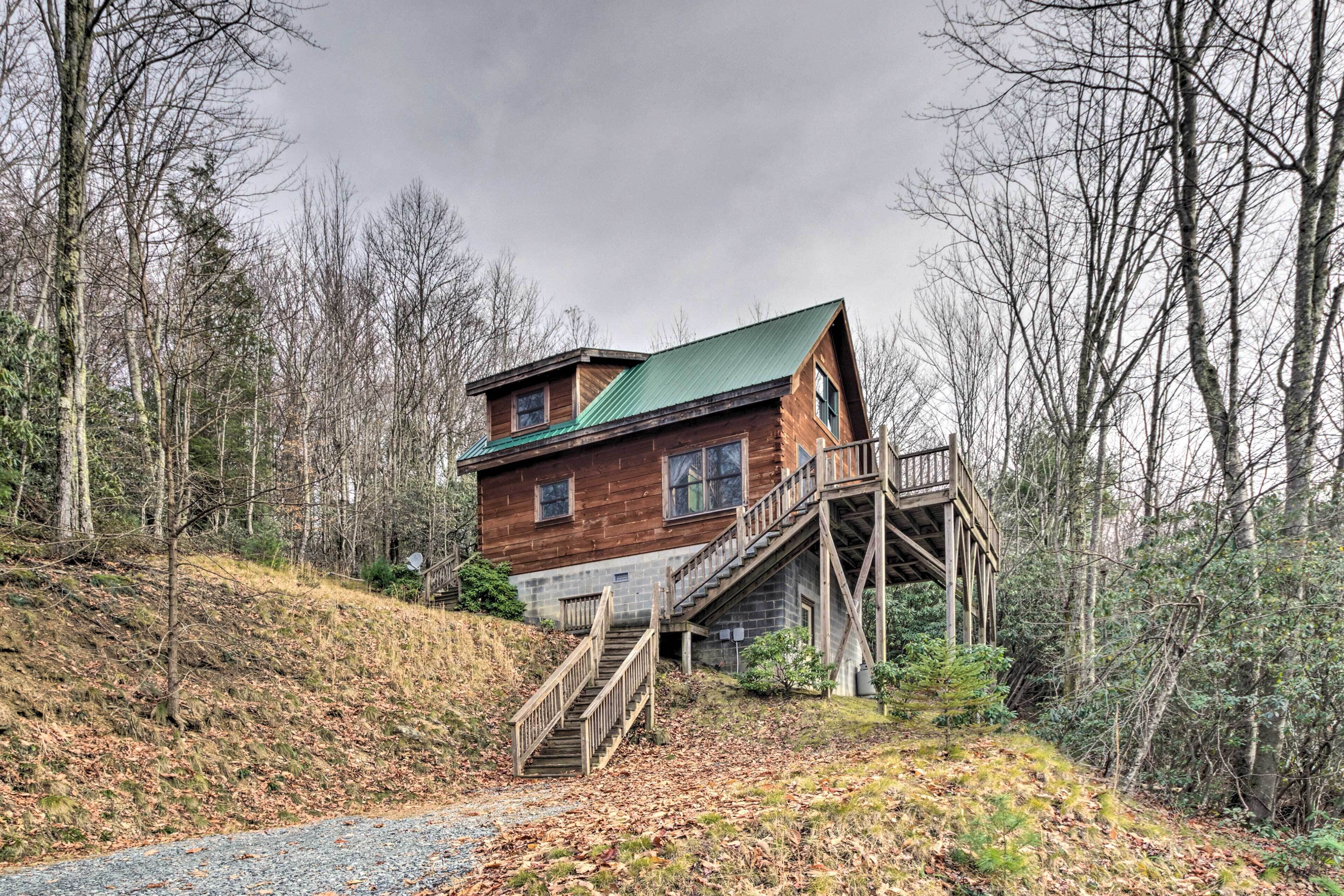 A cabin with a wooden exterior, a green roof, and a wooden staircase leading to a deck.