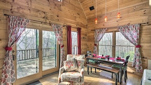 A wooden cabin interior with a dining area, a cushioned armchair, and large windows with curtains. - All-Season Base w/ Scenic Views in Beech Mountain! (Beech Mountain)