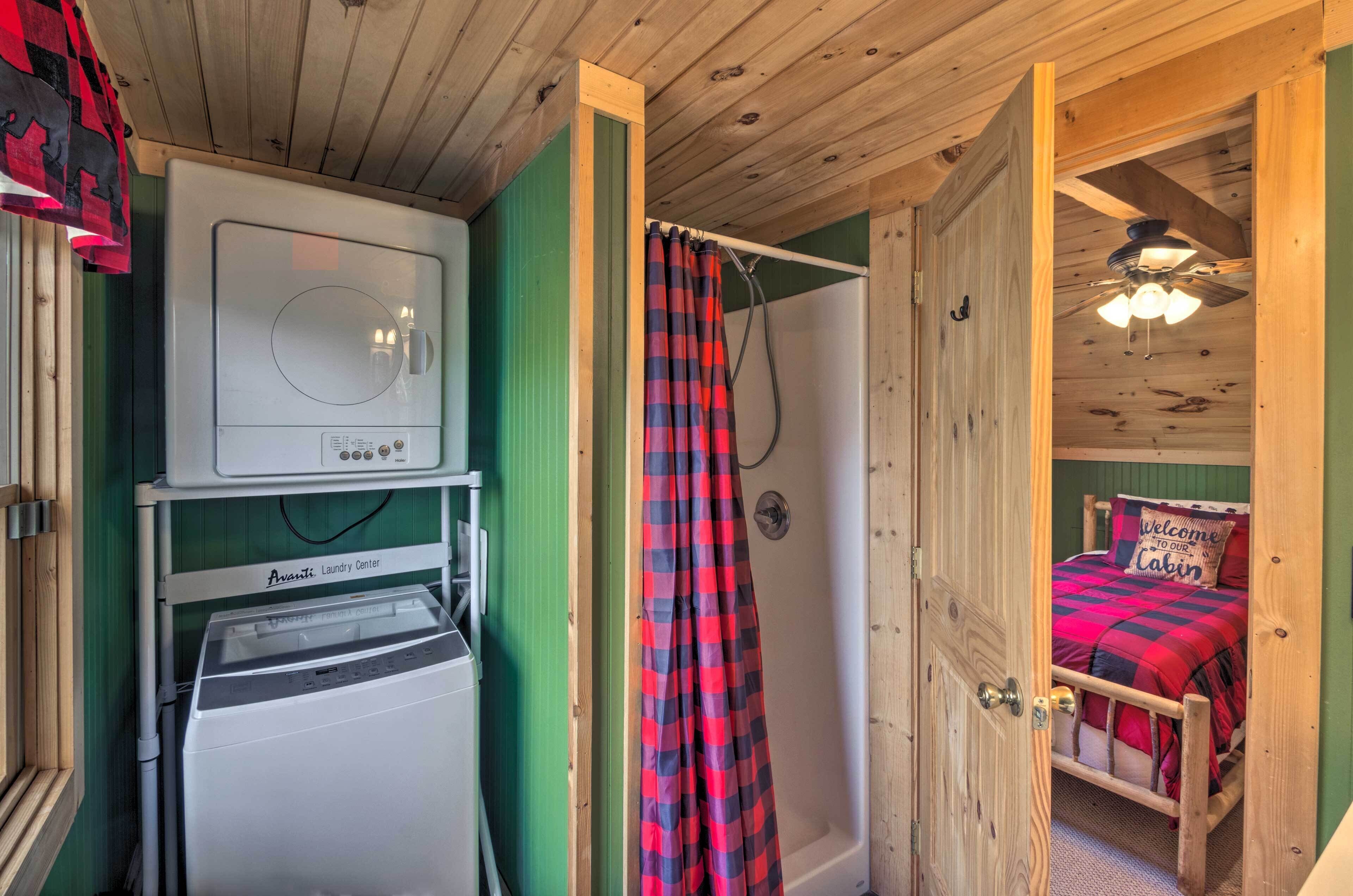 Une pièce avec un lave-linge, une douche dotée d’un rideau à carreaux, et un lit recouvert d’une couverture à carreaux rouges et noirs.
