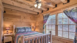 A wooden cabin bedroom with a bed, nightstands, a ceiling fan, and large windows. - All-Season Base w/ Scenic Views in Beech Mountain! (Beech Mountain)