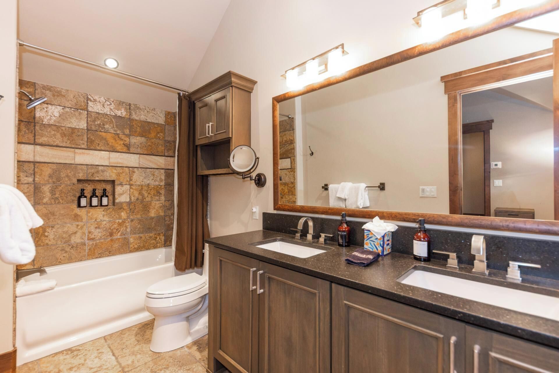 Un baño con bañera, inodoro, un espejo grande y tocador con dos lavabos.