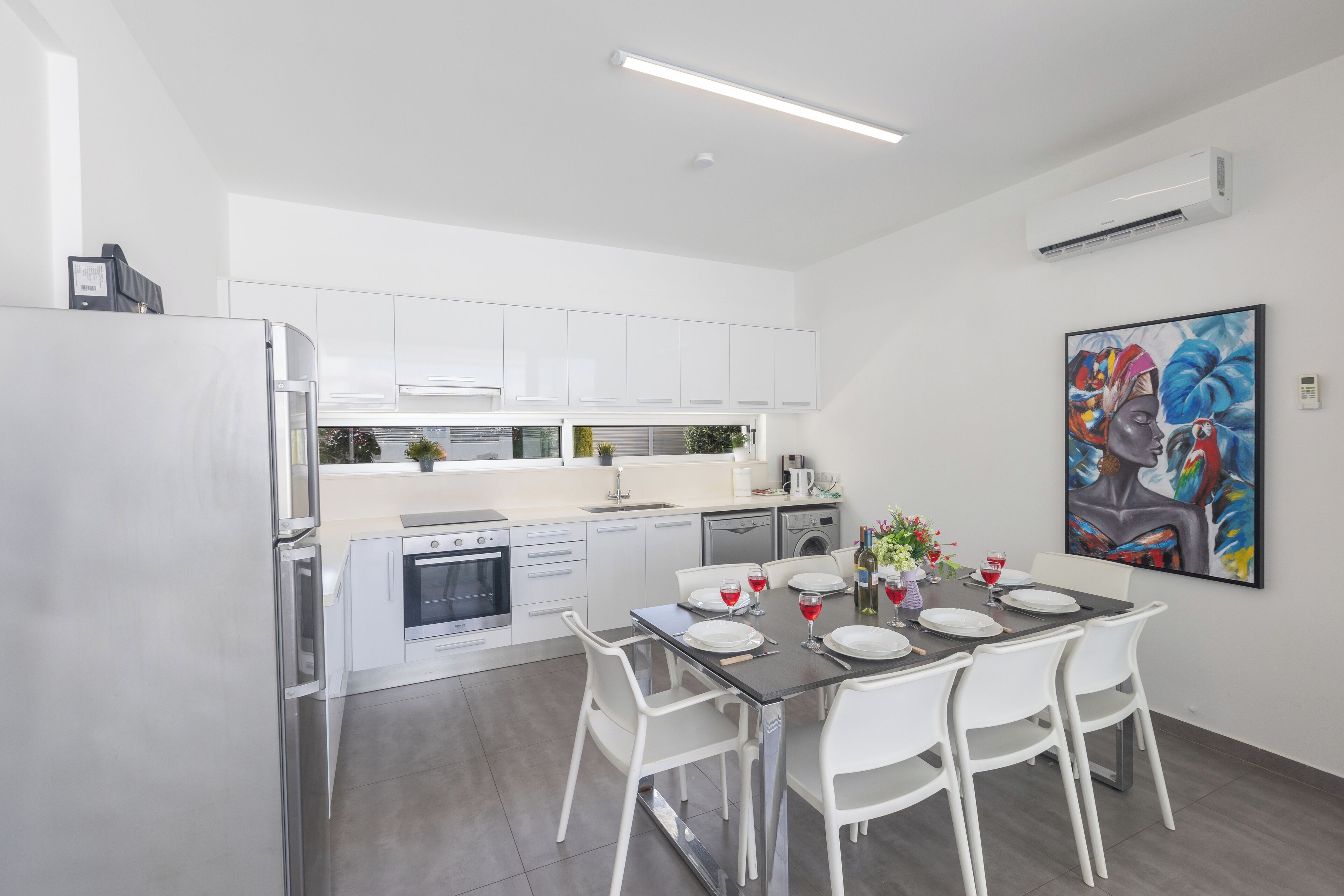 A modern kitchen with white cabinets, a dining table set for four, and a large painting on the wall.