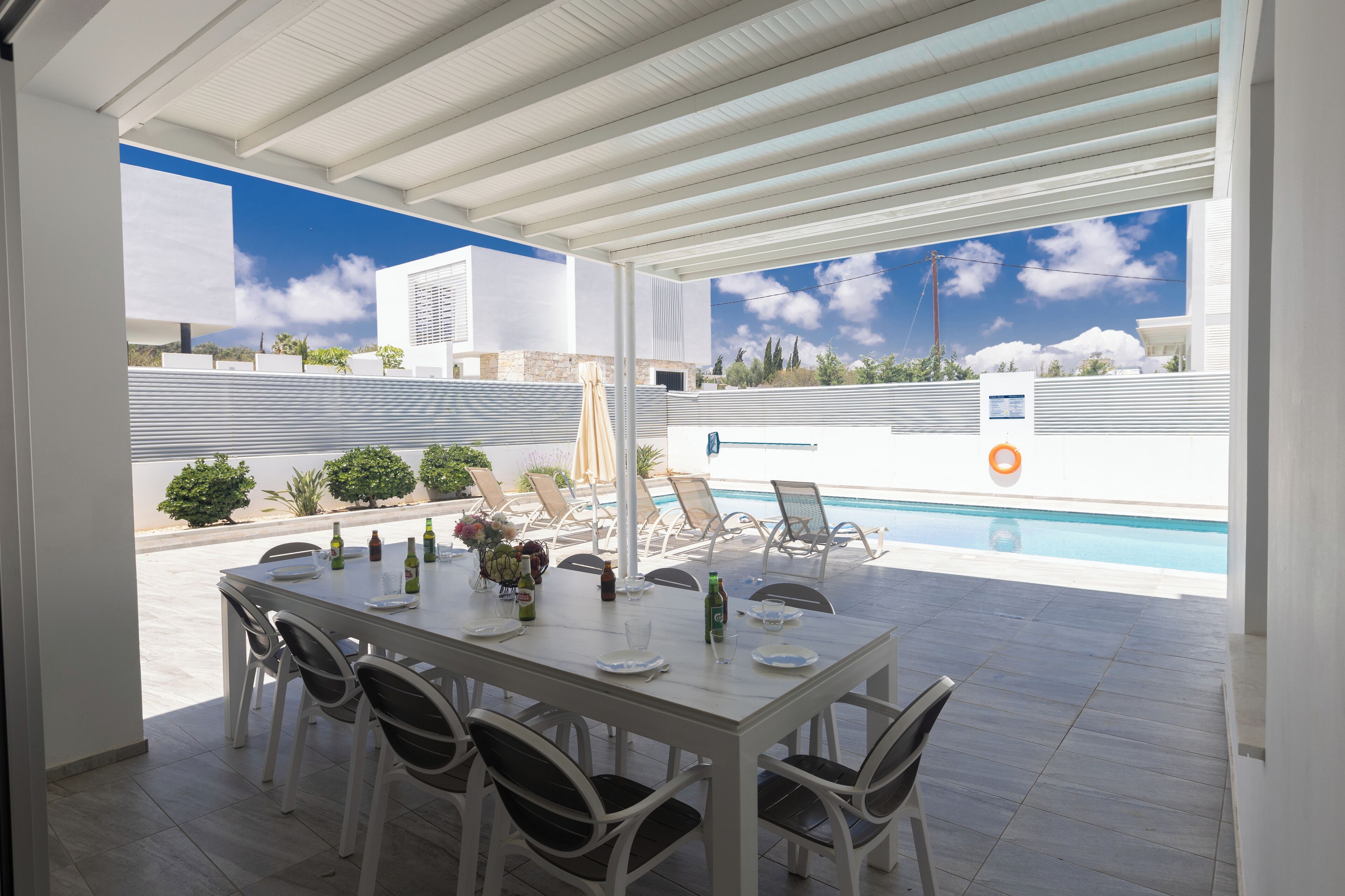 Un área de comedor al aire libre techada, con una piscina al fondo.