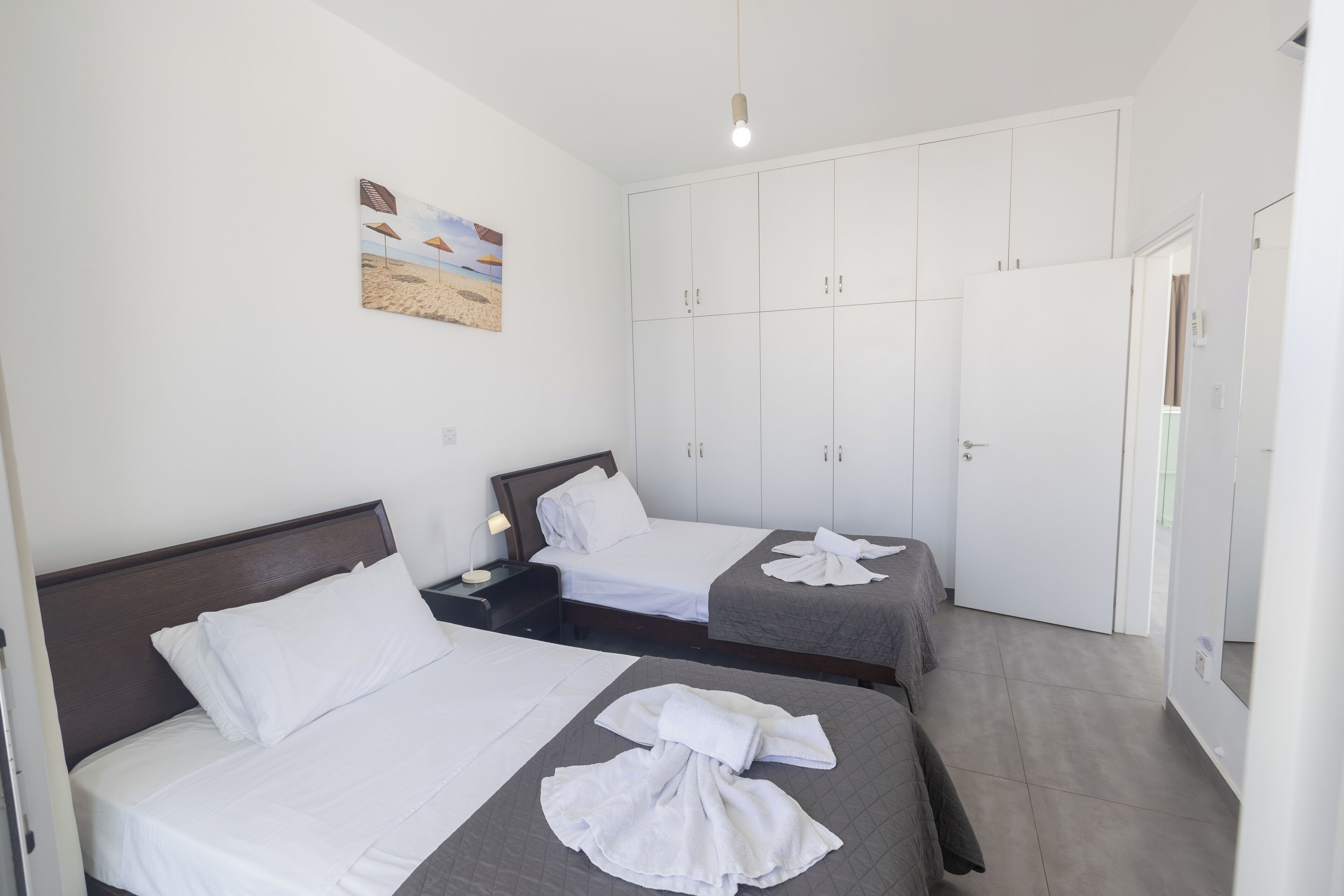 A hotel room with two beds, a wardrobe, and a painting on the wall.
