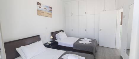 A hotel room with two beds, a wardrobe, and a painting on the wall.