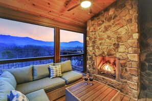 A cozy room with a stone fireplace, a sofa with cushions, and a view of mountains through large windows.