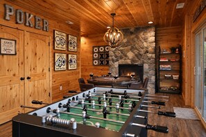 A room with a foosball table, wooden walls, a fireplace, and various framed poker-related artwork.