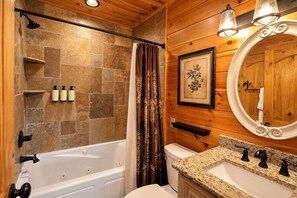 Ein Badezimmer mit einer Steinwand, einer Badewanne, einer Toilette, einem Waschbecken und einem Spiegel.