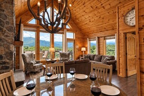 A wooden interior with a dining table set for four, a chandelier, and a view of mountains.
