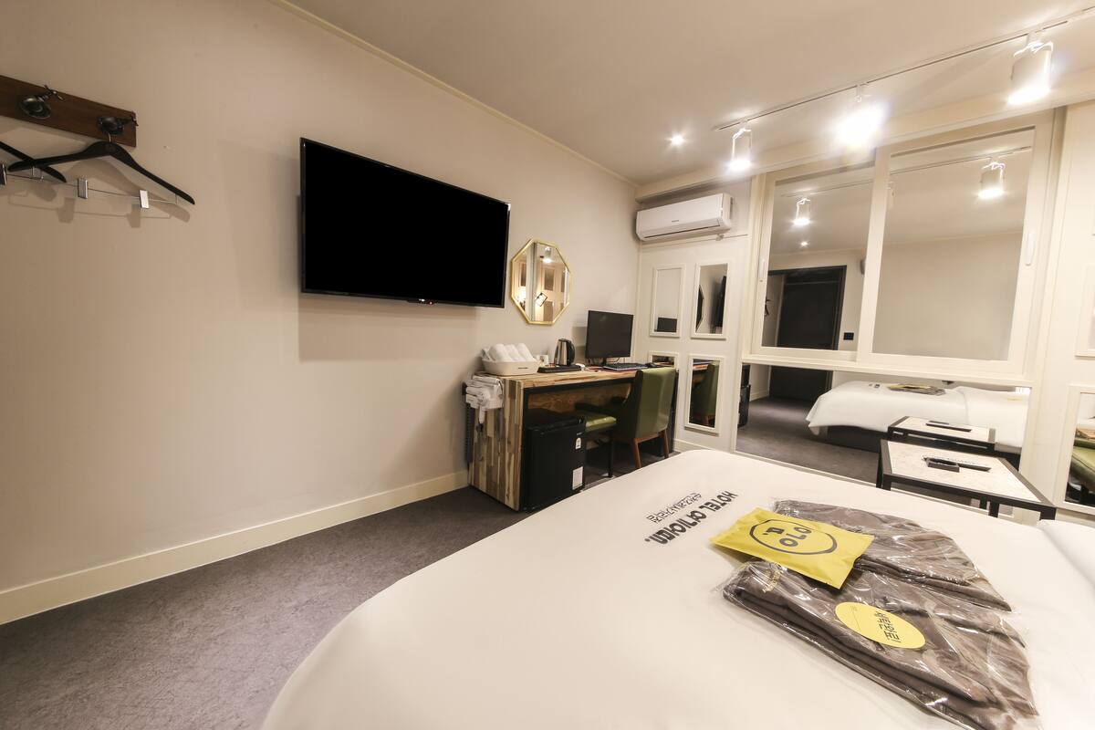 A hotel room with a bed, a desk, a chair, a television, and a mirror.