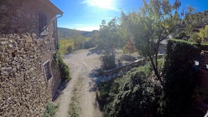 Un bâtiment en pierre à l’aspect rustique, un chemin de terre serpentant à travers un paysage rural et un ciel bleu dégagé.