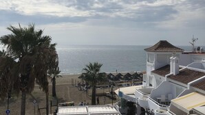 Een kustgebied met strandparasols, palmbomen en uitzicht op zee.