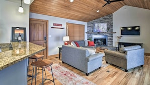A spacious living area with a stone fireplace, a large gray sofa, and a bar area with stools. - Cabin w/ Fireplace & Mountain Views: 5 Mi to Boone (Blowing Rock)