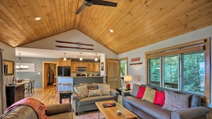 A spacious living area with a high ceiling, wooden beams, a sofa, a coffee table, and a view of the outdoors through large windows. - Cabin w/ Fireplace & Mountain Views: 5 Mi to Boone (Blowing Rock)