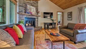 A cozy living room with a stone fireplace, wooden ceiling, and a large flat-screen TV. - Cabin w/ Fireplace & Mountain Views: 5 Mi to Boone (Blowing Rock)