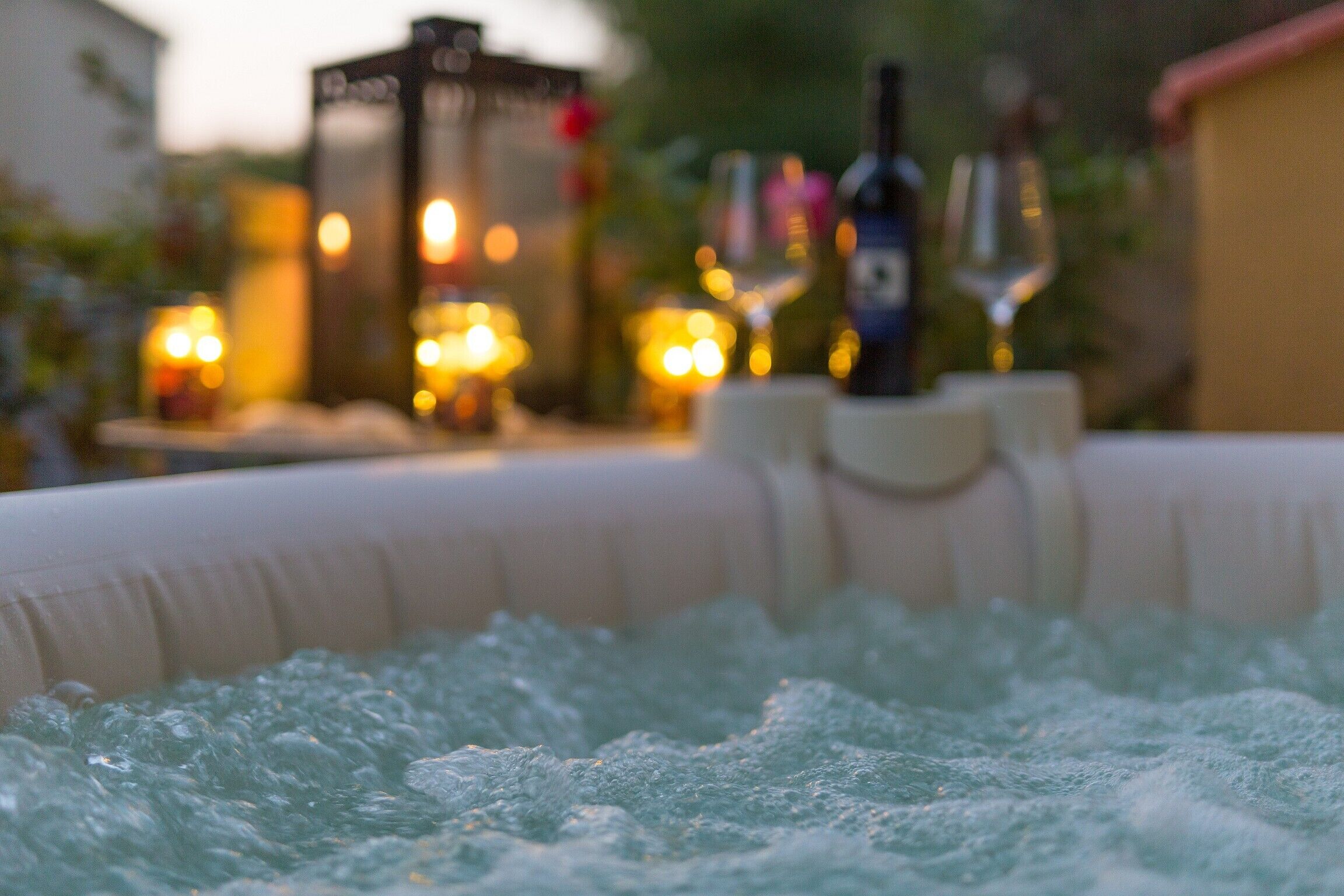 A hot tub with bubbles, surrounded by bottles and glasses, suggesting a relaxing outdoor setting.