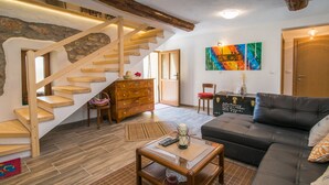 Una sala de estar con una escalera de madera, un sofá de cuero negro, una mesa de centro de madera y un cuadro en la pared.