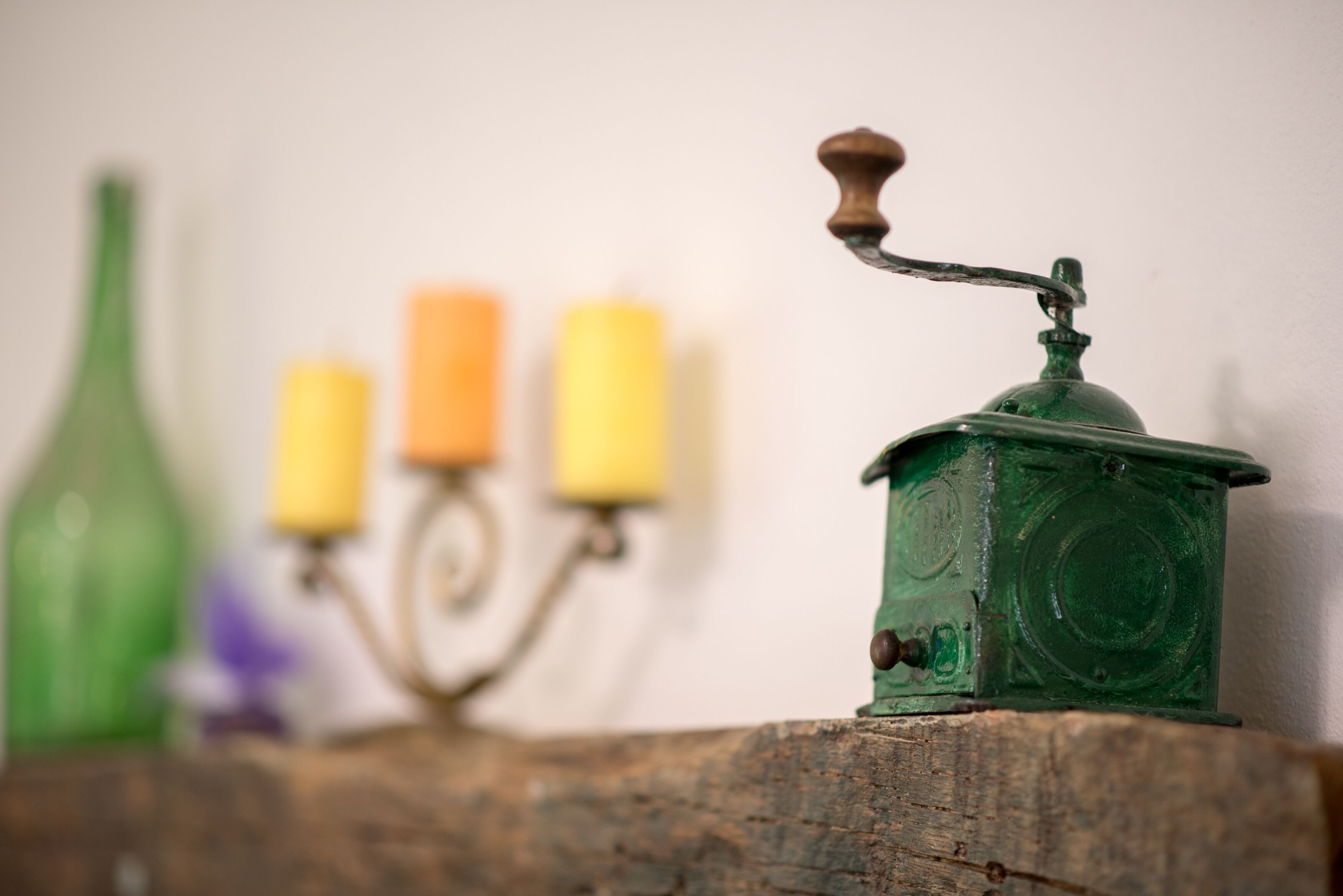 Superficie de madera rústica con un molinillo verde y tres velas al fondo.