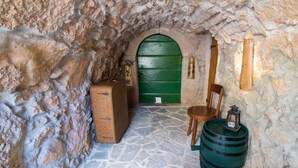Una habitación con paredes de piedra, una puerta verde, un cofre de madera, una silla y un barril.