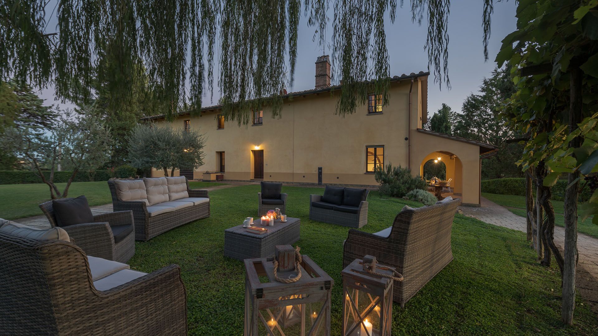 Un patio con mobiliario de mimbre, una chimenea y un edificio con entrada iluminada.
