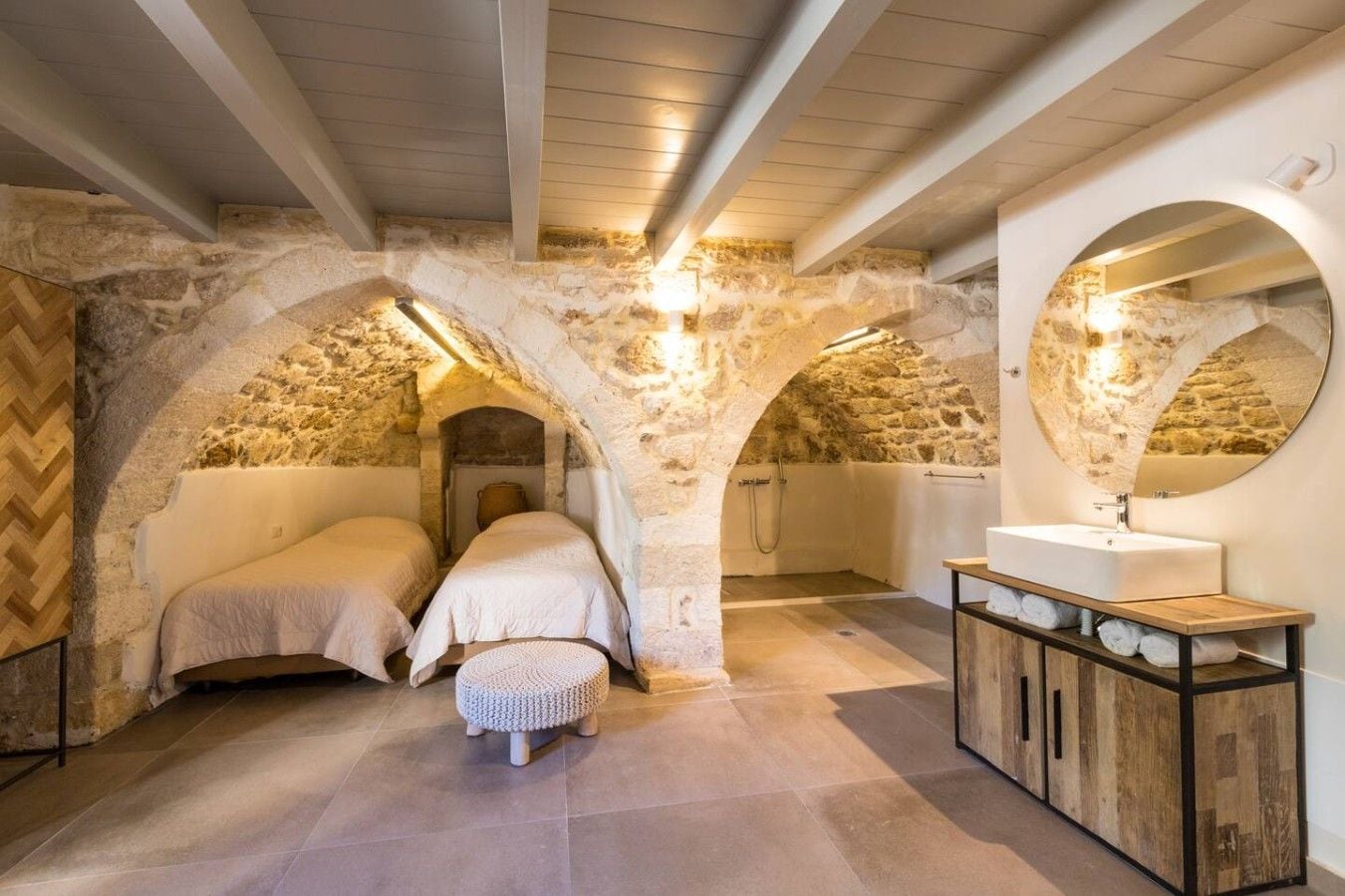 A stone-walled bedroom with two beds, a wooden bench, and a large mirror.