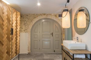A bathroom with a wooden herringbone floor, a grey arched door, a white sink, and two pendant lights.