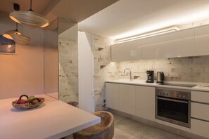 A modern kitchen with a white countertop, stainless steel appliances, and a basket of fruit on the table.