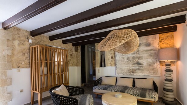 Un salon chaleureux avec un mur en pierre, un luminaire suspendu en fibres tressées, un ensemble de canapés, une table basse ronde et un grand lampadaire.