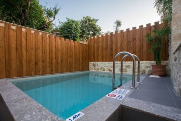 A swimming pool with a wooden fence, a stone wall, and a metal ladder.