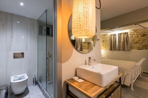Un baño moderno con cabina de ducha de vidrio, un lavamanos blanco y encimera de madera, y una pared de piedra.