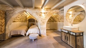 Une chambre avec une arche en pierre, un lit, une armoire en bois contenant des serviettes et un miroir rond.