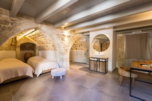 Un dormitorio con paredes de piedra, una cama de madera, un espejo redondo y una mesita.