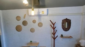 Ein Zimmer mit einem Holztisch, zwei Hocker, einem Kleiderhaken, einem Spiegel und mehreren gewebten Körben an der Wand.