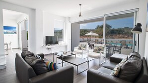 A modern living room with a large sliding glass door leading to an outdoor area with a pool and lounge chairs. - Villa Kylee, Fabulous 5BDR Protaras Villa with private pool, close to the beach (Protaras)