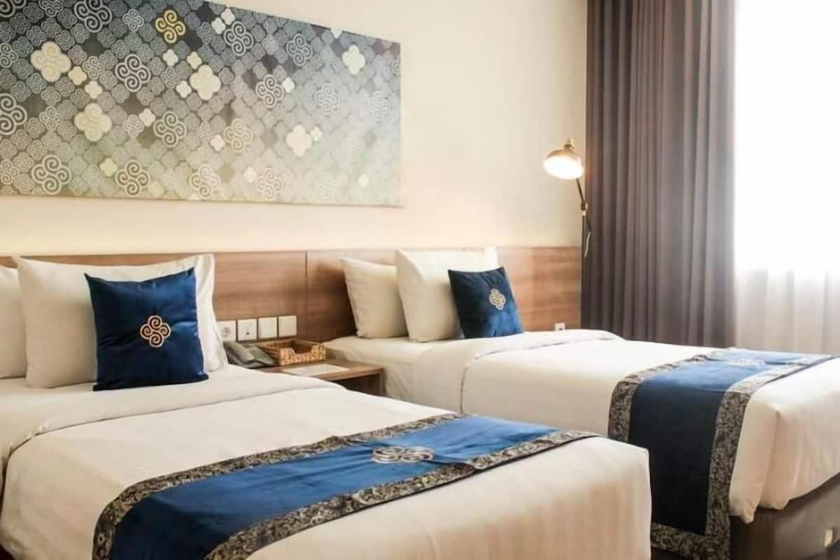 A hotel room with two beds, a nightstand, a lamp, and a patterned wall.