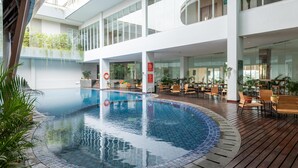 Et moderne poolområde indendørs med træterrasse, siddepladser og glasvægge.