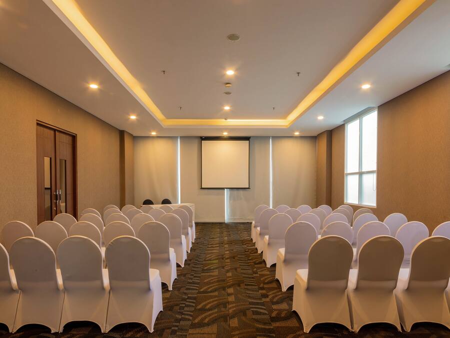 Ein Konferenzraum mit Reihen weißer Stühle, einer Projektionsleinwand und einem Teppichboden.
