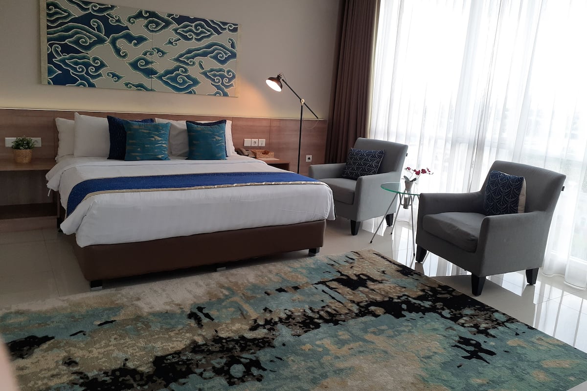 A hotel room with a large bed, a desk, a chair, and a large window with curtains.