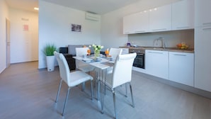 Een moderne keuken met witte kastjes, een eethoek met een tafel gedekt voor twee personen, en een kleine potplant.