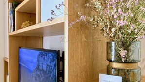 A wooden shelf with a television displaying a mountainous landscape, a vase with dried flowers, and a sign reading "HOME Chic HOME". - Les Toits de Sainte-Ursule (Montpellier)
