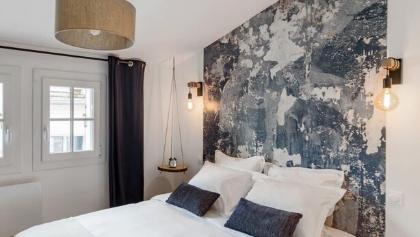 A bedroom with a large bed, a rustic wall, and a hanging light fixture. - Les Toits de Sainte-Ursule (Montpellier)