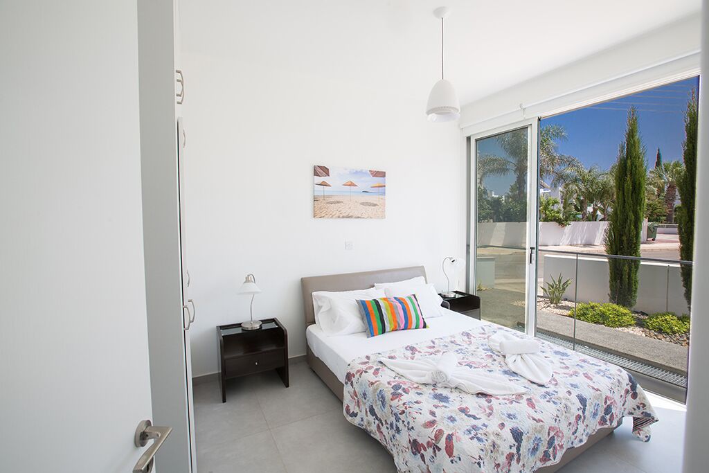 Une chambre moderne avec un grand lit, une vue sur l’extérieur et un tableau sur le thème de la plage accroché au mur.
