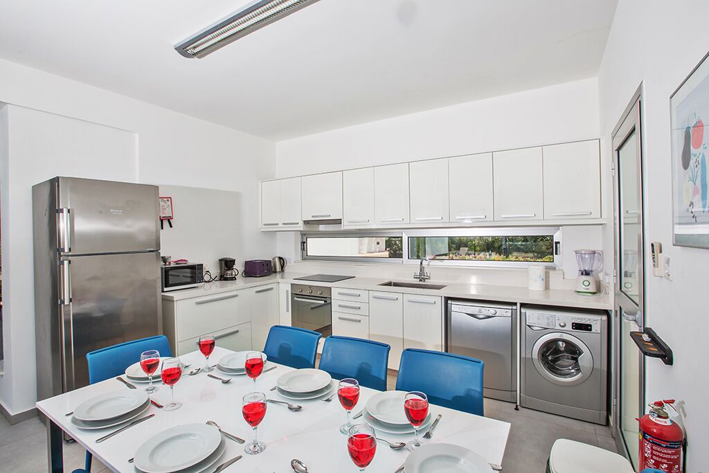 A modern kitchen with white cabinets, a stainless steel refrigerator, a microwave, a sink, a dishwasher, and a washing machine.