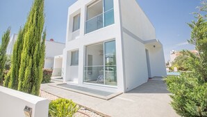 Une maison moderne à deux étages, dotée de grandes fenêtres et d’un toit plat.