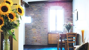 A room with a stone wall, a window, a dining table with chairs, and a bed with a patterned pillow. - Charming apartment in Navona Square (Multiple rentals available) (Roma)