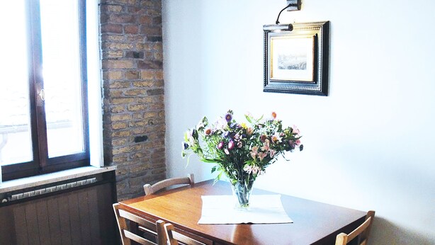 A dining table with a vase of flowers, wooden chairs, a brick wall, and a framed picture on the wall. - Charming apartment in Navona Square (Multiple rentals available) (Roma)